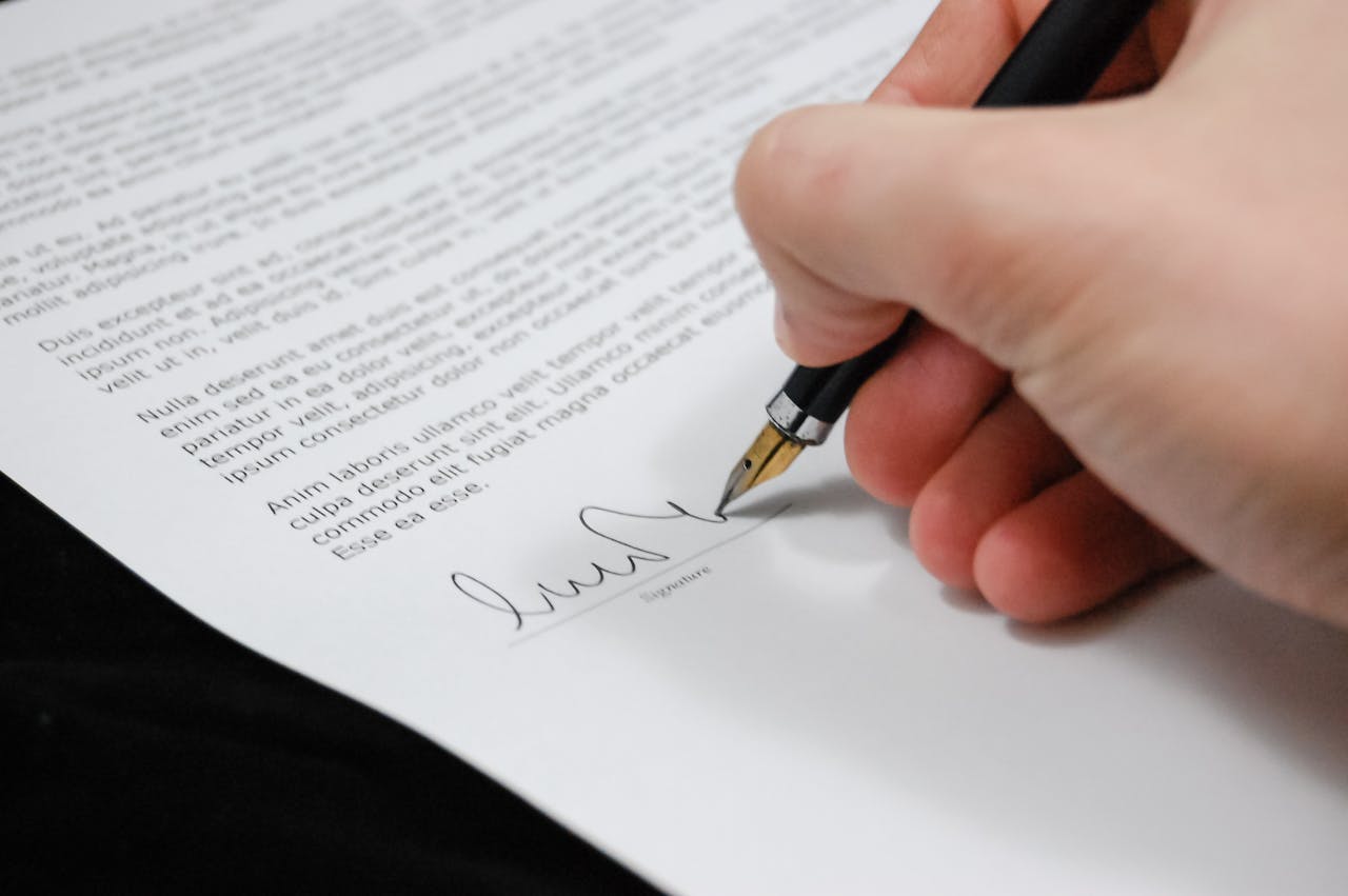 Offerings Close-up of a hand signing a legal document with a fountain pen, symbolizing signature and agreement.