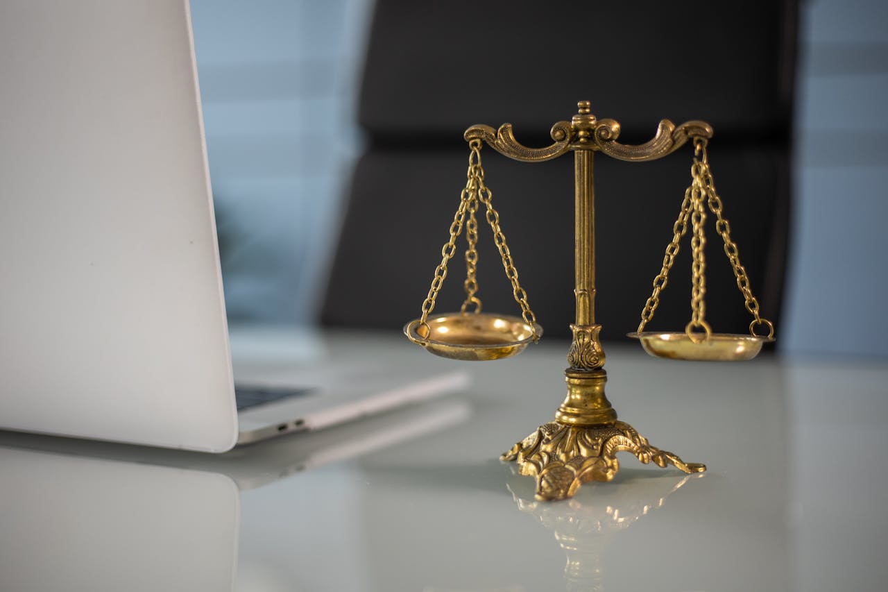Offerings Golden justice scales on a desk beside a laptop, symbolizing law and balance.